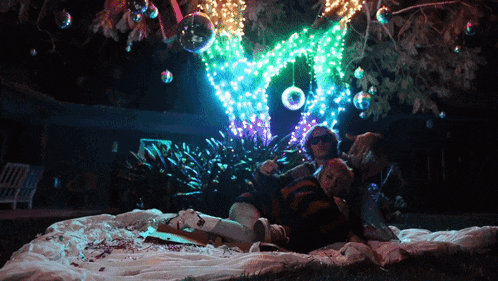 a group of people laying under a tree with christmas lights on it