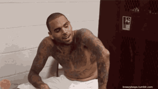 a shirtless man is sitting in front of a locker with a sticker that says ' a ' on it