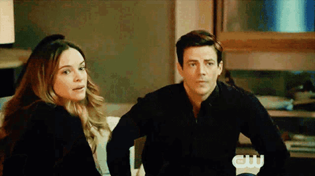 a man and a woman are sitting next to each other in front of a sign that says " cw "