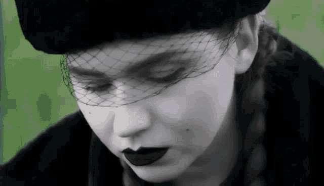 a woman wearing a black hat with a veil on her face is looking down .
