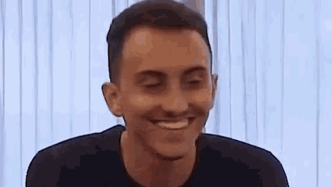 a man in a black shirt is smiling with his eyes closed and his mouth open .