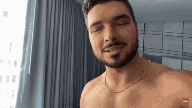 a shirtless man with a beard and a gold chain around his neck