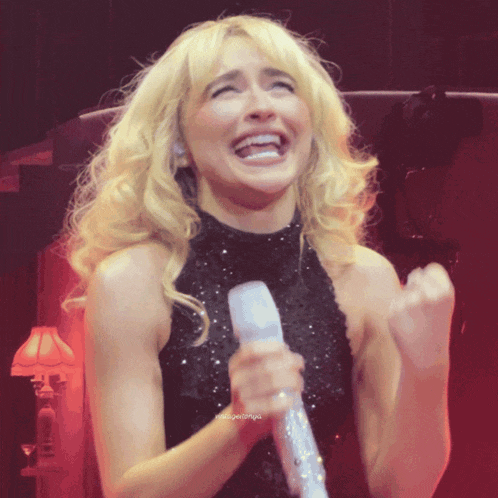 a woman in a black dress is holding a microphone and making a funny face