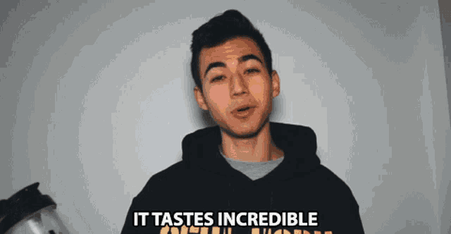 a young man in a black hoodie with the words it tastes incredible behind him