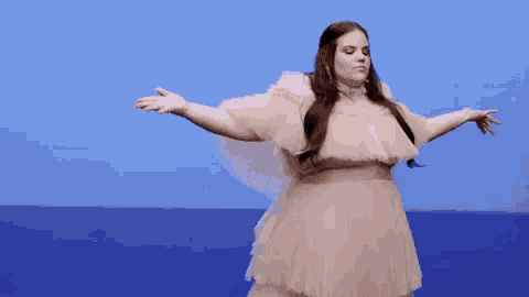 a woman in a white dress is standing with her arms outstretched in front of a blue sky .