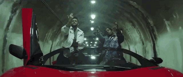 two men are riding in a red sports car in a tunnel .