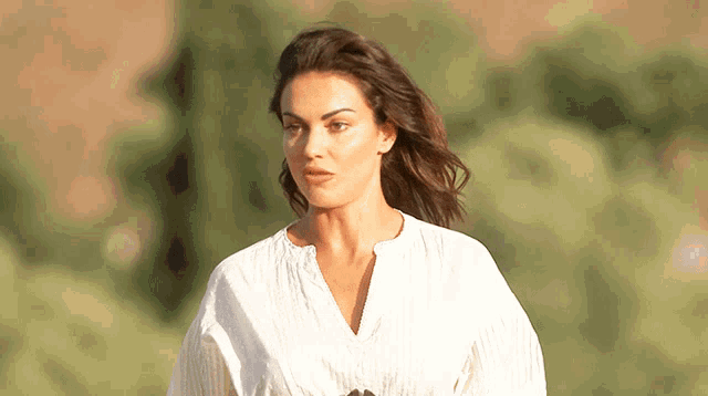 a woman wearing a white shirt stands in a field