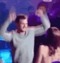 a man is dancing in a club with his arms in the air and a woman is standing behind him .