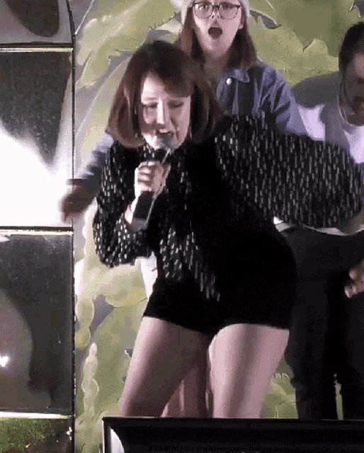 a woman singing into a microphone in front of a wall