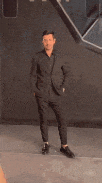 a man in a suit leans against a wall
