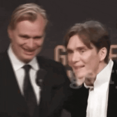 two men in suits and ties are standing next to each other on a red carpet and smiling .