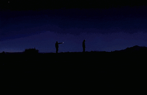 two people standing in front of a full moon in the dark
