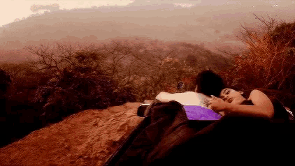 a man and a woman are laying in a tent on a hillside