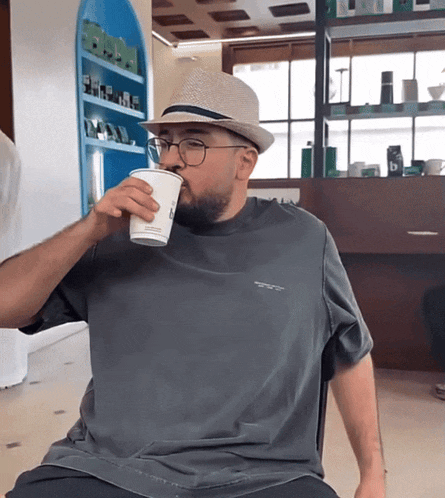 a man wearing a hat and glasses is drinking from a cup that says ' arabica ' on it