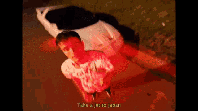a man is standing in front of a car with the words `` take a jet to japan '' written on the bottom .