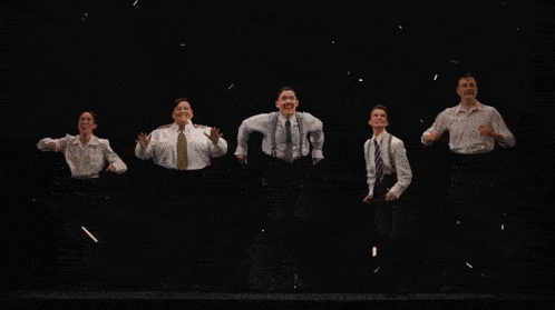 a group of men are jumping in the air with their arms in the air and red petals falling around them