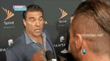 a man is talking into a microphone while another man watches .