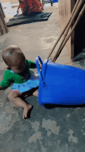 a baby is playing with a blue bucket on the ground