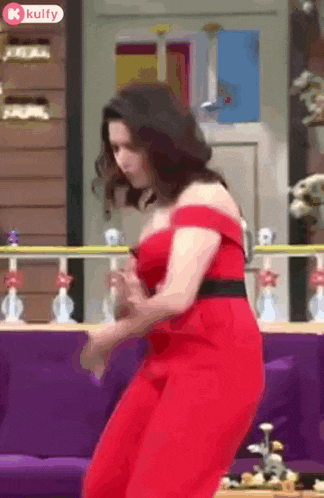 a woman in a red dress is dancing on a couch in front of a purple couch .