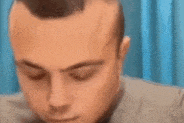 a close up of a man 's face with his eyes closed and a blue curtain behind him .