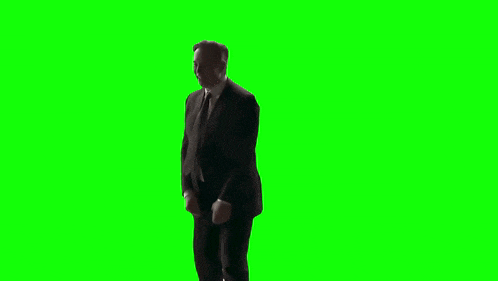 a man in a suit and tie is dancing on a green screen while holding a cell phone .