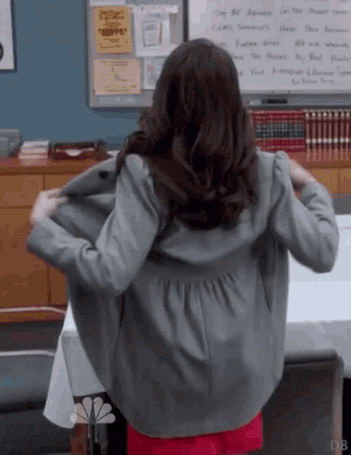 a woman in a grey jacket is standing in front of a table with her arms outstretched