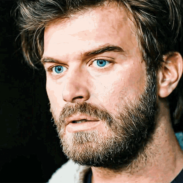 a man with a beard and blue eyes looks to the side