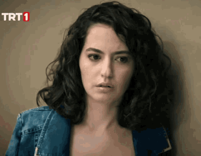 a woman in a denim jacket stands in front of a wall with trt1 written on the bottom