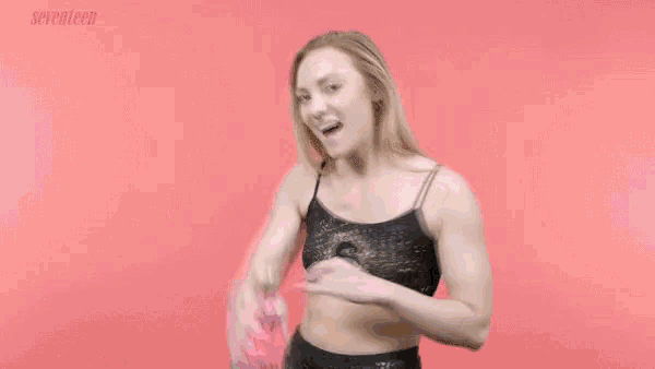 a woman in a black top with the letter s on it is holding up a pink water bottle