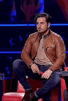 a man in a brown leather jacket sits on a chair