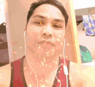 a man wearing ear buds and a red tank top is taking a selfie