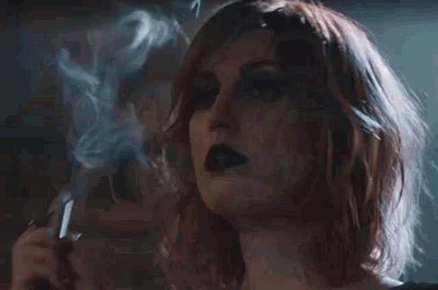 a woman with red hair is smoking a cigarette in a room .
