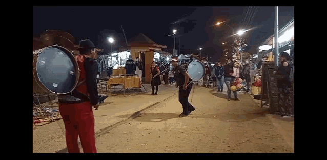 a group of people are playing drums on a street at night
