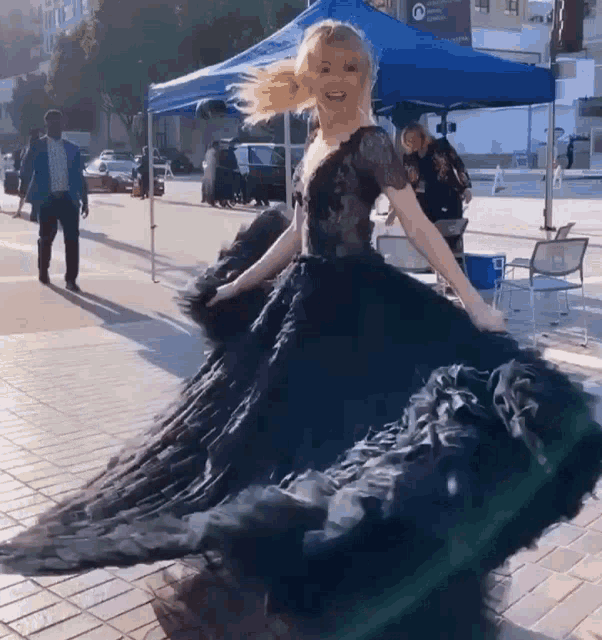 a woman in a black dress is dancing on a sidewalk in front of a blue tent