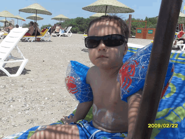a young boy wearing sunglasses is sitting on a beach with the date 2009/02/20