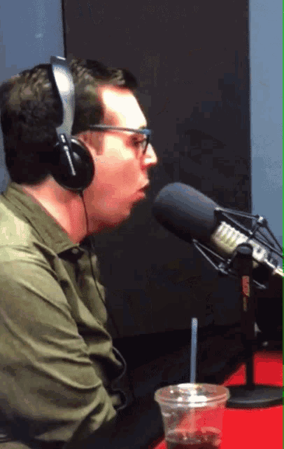 a man wearing headphones talking into a microphone with a cup of coffee in front of him