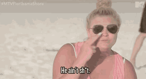 a woman wearing sunglasses and a pink tank top is standing on a beach and saying he ain 't shit .