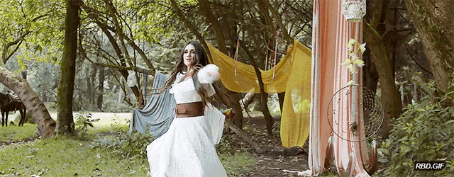a woman in a white dress is dancing in a forest with a horse in the background