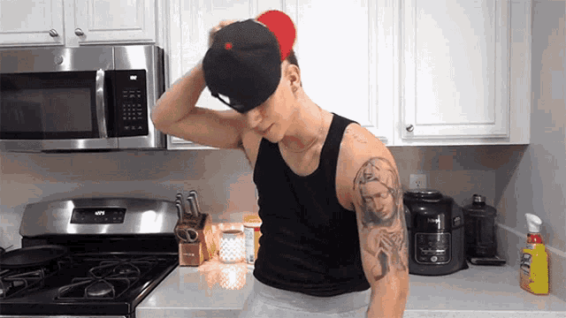 a man with a tattoo on his arm is standing in a kitchen wearing a hat