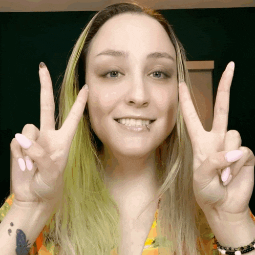 a woman with green hair makes a peace sign