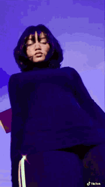 a woman in a black shirt is standing in front of a blue background with tiktok written in the corner