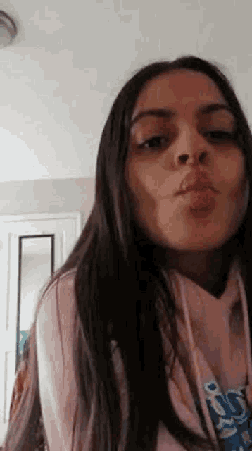 a woman is blowing a kiss while wearing a pink hoodie .