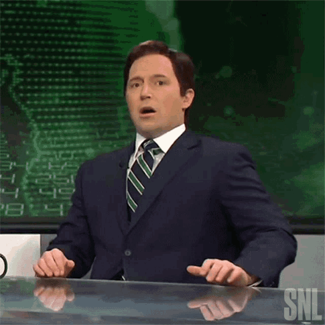a man in a suit and tie is sitting in front of a snl logo