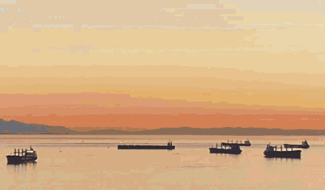 several ships are floating in the water at sunset