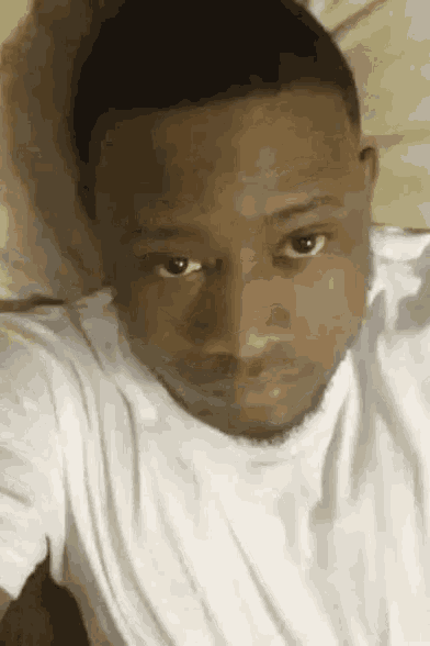 a man in a white shirt is laying on a bed with his head on a pillow .