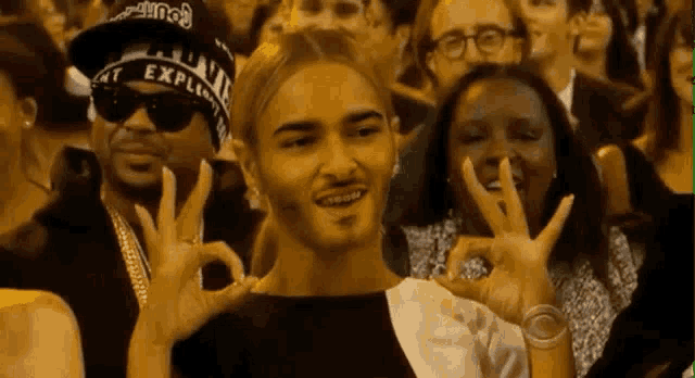 a man wearing a hat with the word explain on it is giving the ok sign