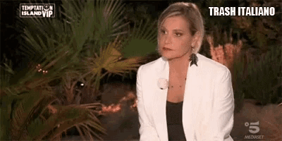 a woman in a white jacket is sitting in front of a palm tree on a television show .