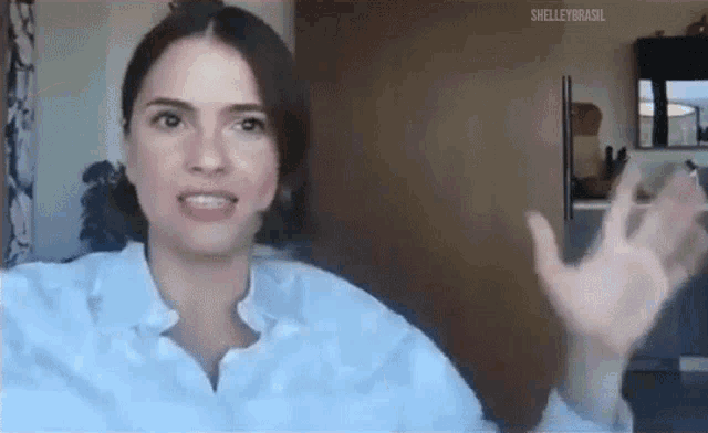 a woman in a white shirt is sitting in front of a computer and waving her hand .