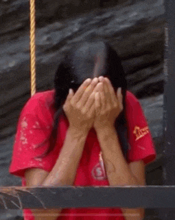 a woman is covering her face with her hands in a red shirt .