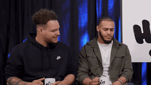 two men are sitting next to each other and one of them is wearing a nike hoodie